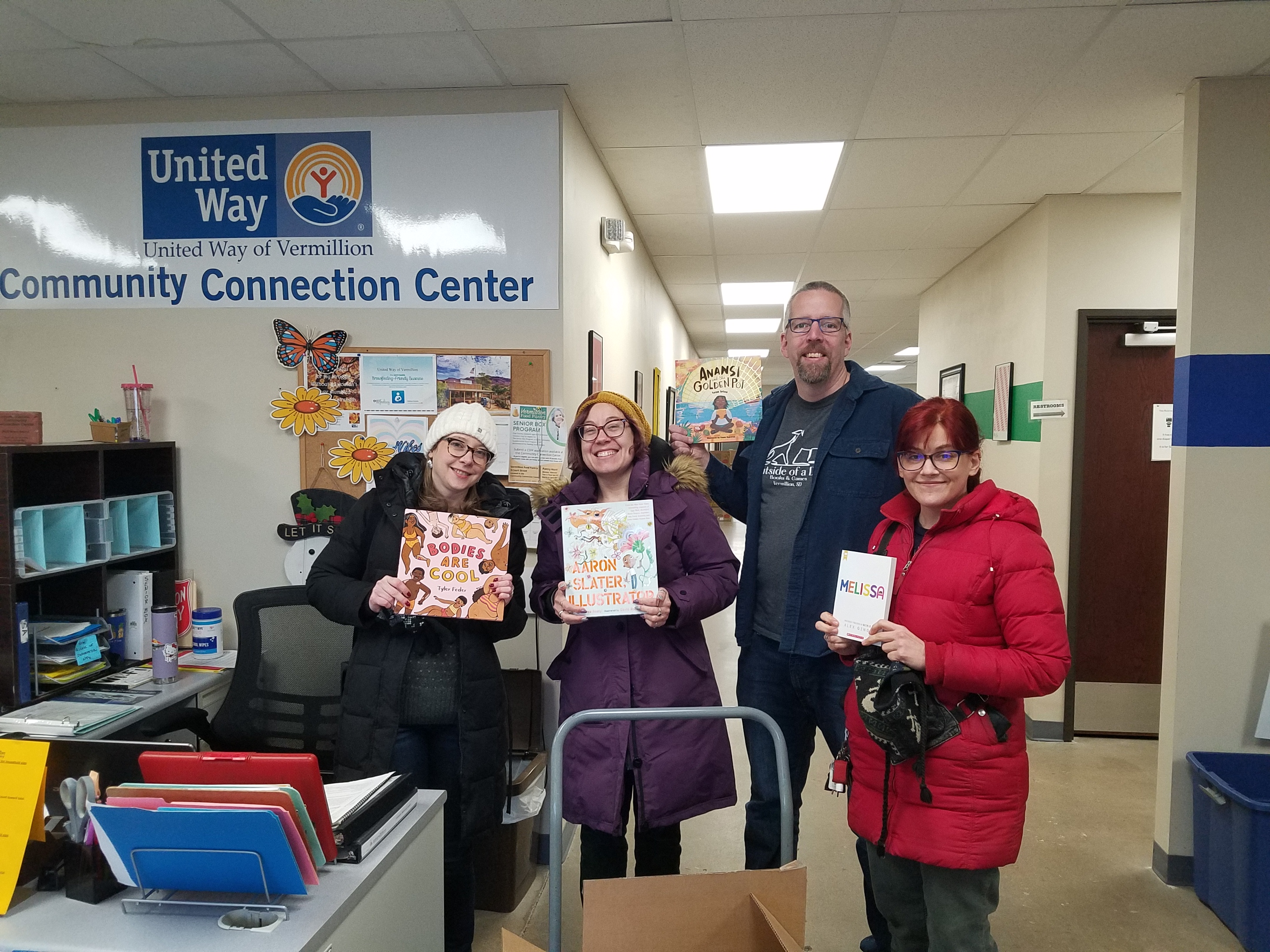 Smiling people holding donated children's books in the United Way Community Connection Center